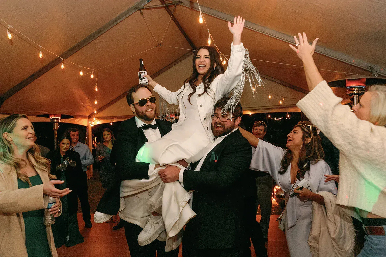 Bride lifted in celebration at reception party with string lights